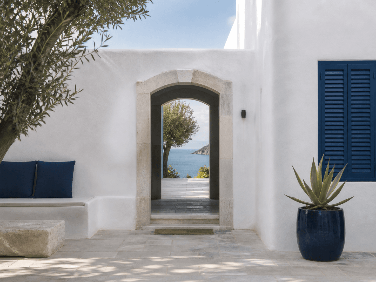 A bright Portuguese coastal hotel courtyard with white walls, blue shutters, and a sea view